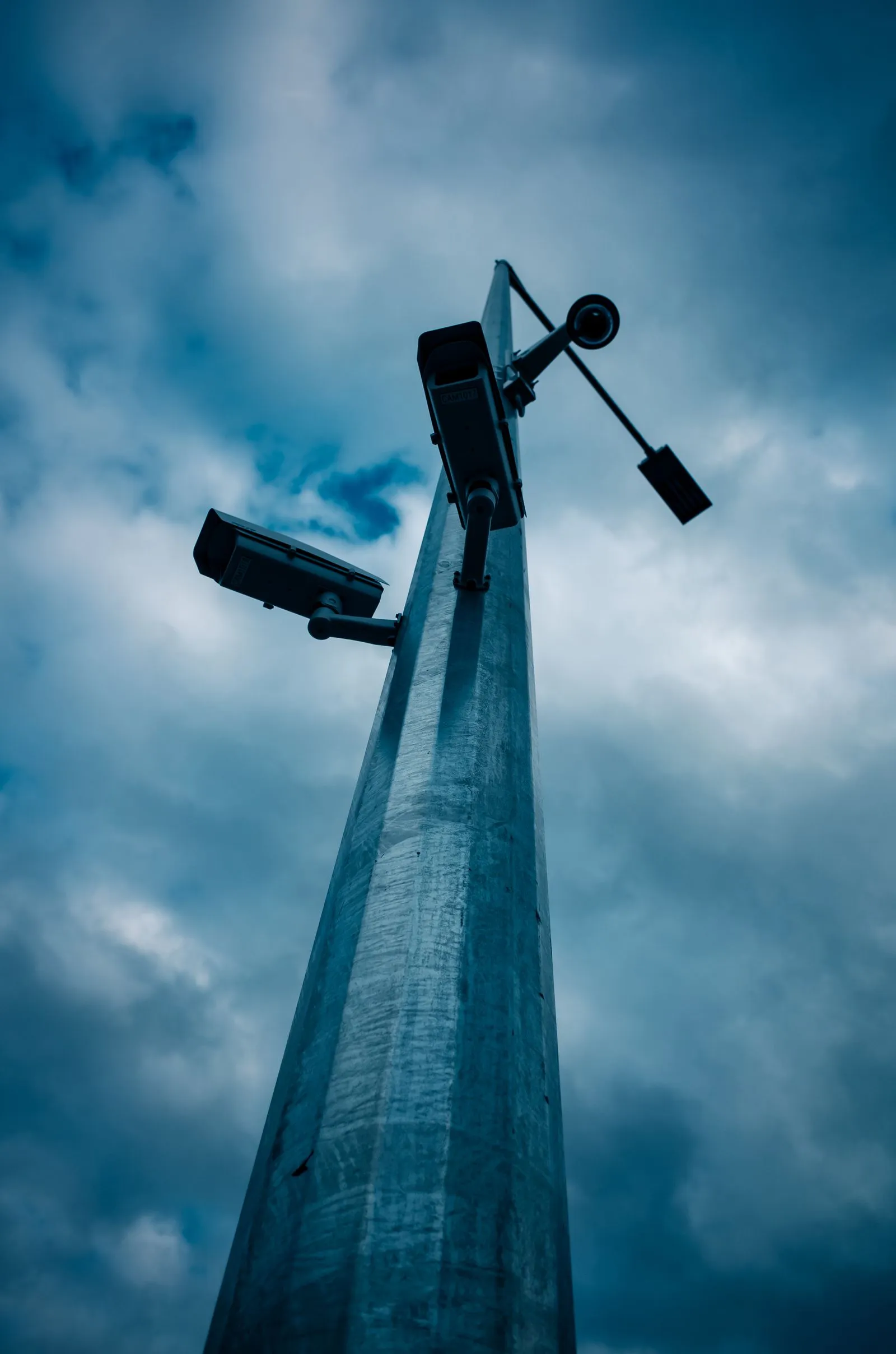 Tall pole with two CCTV cameras monitoring an industrial site against a dramatic sky